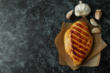 Izgara tavuk göğsü ve siyah dumanlı arka planda sarımsak.