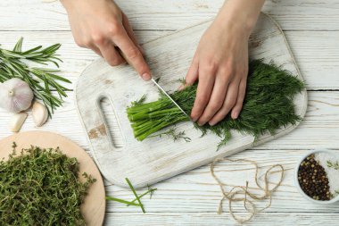 Kadın eli, beyaz ahşap arka planda dereotu kesiyor.