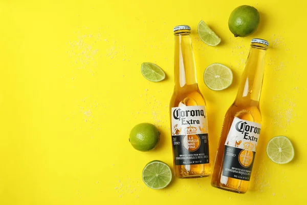 Bottles of Corona Extra, limes and salt on yellow background