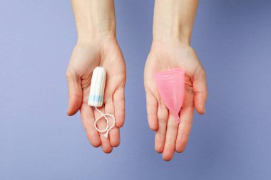 Kadın elleri menekşe arka planında regl bardağı ve tampon tutuyor.