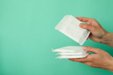 Kadın elleri arka planda hijyen pedlerini tutar.