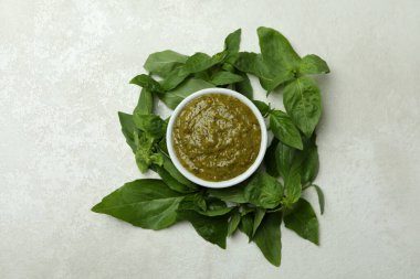 Beyaz desenli arka planda bir kase Pesto sosu ve fesleğen