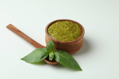 Beyaz arka planda bir kase Pesto sosu, fesleğen ve kaşık.