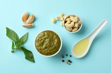 Bir kase Pesto sosu ve mavi arka planda malzemeler.