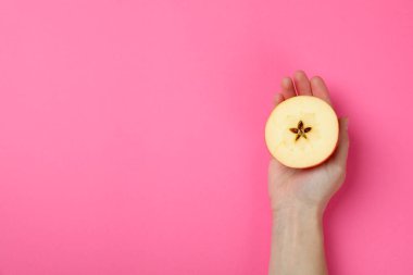 Kadın eli, pembe arka planda bir elma dilimi.