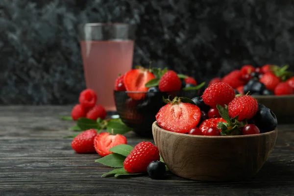 Bowls with berry mix and juice on wooden table