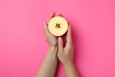 Kadın elleri pembe arka planda elmayı tutuyor.