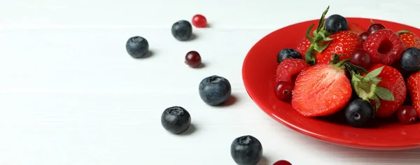 Plate with berry mix on white wooden background