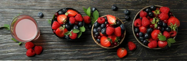 Bowls with berry mix and juice on wooden background
