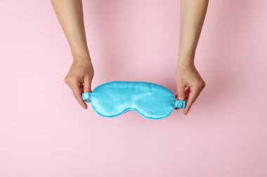 Kadın elleri pembe arka planda uyku maskesi tutuyor