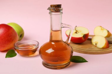 Ev yapımı elma sirkesi ve pembe arka planda malzemeler.