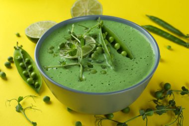 Sarı zemin üzerinde bezelye çorbası ve malzeme tabağı.