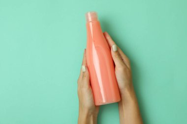 Kadın elleri arka planda boş şampuan şişesi tutuyor.