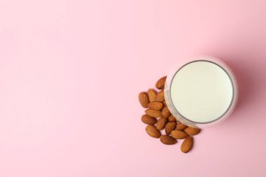 Pembe arka planda bir bardak süt ve badem.