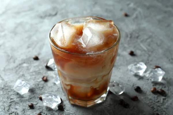 Glass of ice coffee, beans and ice on grey textured table