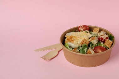 Sezar salatası ve pembe arka planda çatal bıçak takımı.