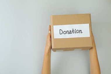 Kadın eli, açık gri arka planda bağış kutusunu tutuyor.