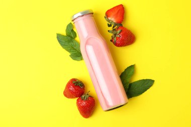 Bir şişe çilekli milkshake ve sarı arka planda malzemeler.
