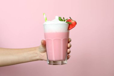 Kadın eli pembe arka planda bir bardak çilekli milkshake tutuyor.