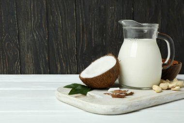 Beyaz ahşap masada bir sürahi süt, hindistan cevizi ve fındık.