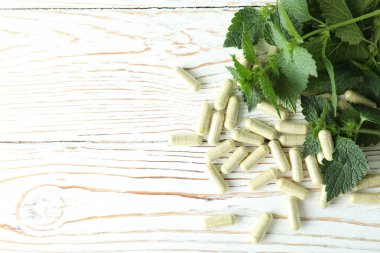 Isırgan otu hapları ve malzemeler beyaz ahşap masada.