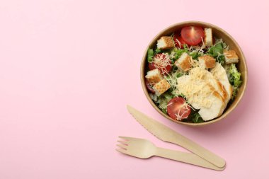 Sezar salatası ve pembe arka planda çatal bıçak takımı.