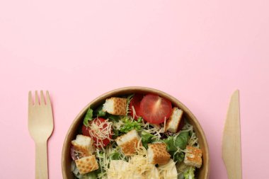 Sezar salatası ve pembe arka planda çatal bıçak takımı.