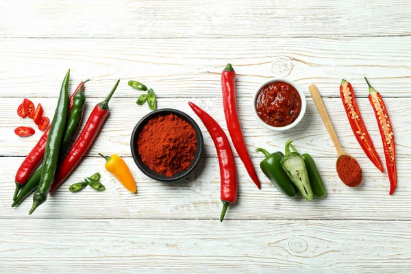 Hot peppers, sauce and powder on white wooden background