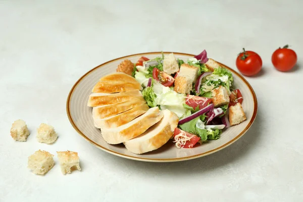 Plate with Caesar salad and ingredients on white textured background