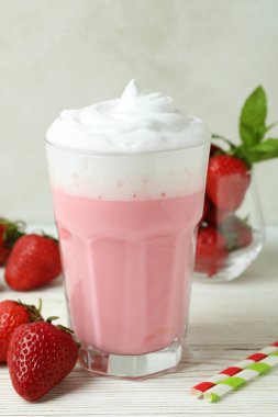 Bir bardak çilekli milkshake ve beyaz ahşap masa malzemeleri.