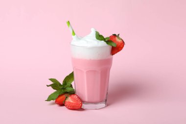 Bir bardak çilekli milkshake ve pembe arka planda malzemeler.