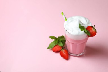 Bir bardak çilekli milkshake ve pembe arka planda malzemeler.