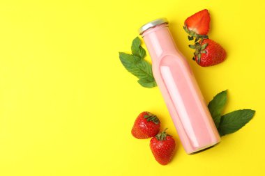 Bir şişe çilekli milkshake ve sarı arka planda malzemeler.