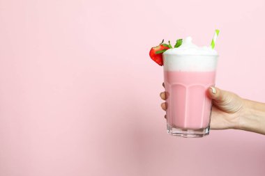 Kadın eli pembe arka planda bir bardak çilekli milkshake tutuyor.