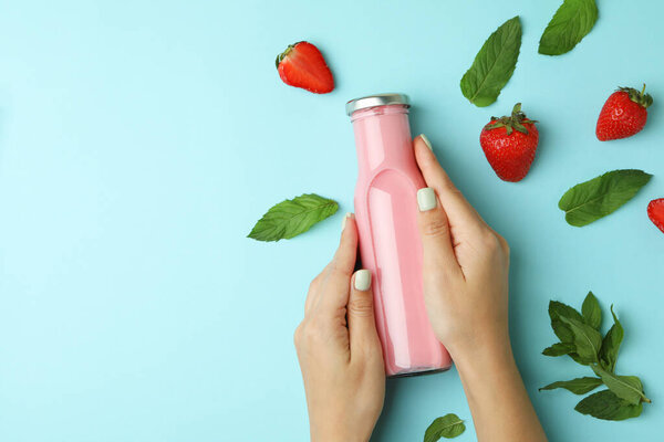 Female hands holding bottle of strawberry milkshake on blue background