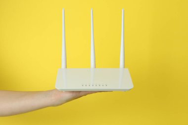 Kadın eli sarı arkaplanda Wi-fi yönlendiricisi tutuyor.