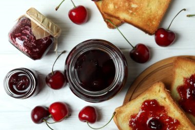 Kiraz reçeli ve malzemeler beyaz ahşap masada.