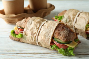 Ciabatta sandviçleri ve kahve fincanları beyaz ahşap masada.