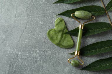 Yüz silindiri, gua sha ve gri desenli arka planda dal