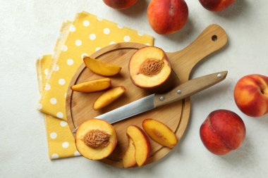 Beyaz desenli masa üzerinde şeftali meyveleri, bıçak ve mutfak havlusu.