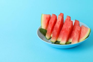 Mavi zemin üzerinde karpuz dilimleri ve nane yapraklarıyla kaplı bir tabak.