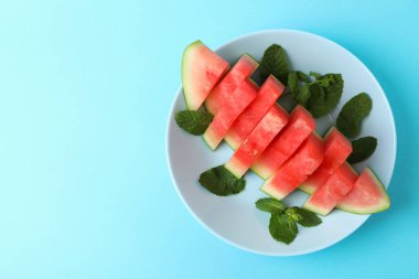 Mavi zemin üzerinde karpuz dilimleri ve nane yapraklarıyla kaplı bir tabak.