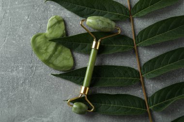 Yüz silindiri, gua sha ve gri desenli arka planda dal