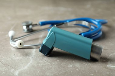 Astım spreyi ve steteskop gri desenli masada.