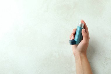 Kadın eli beyaz desenli masada mavi astım spreyini tutuyor.