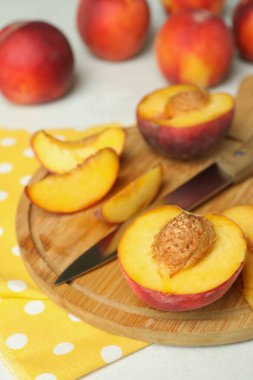 Beyaz desenli masa üzerinde şeftali meyveleri, bıçak ve mutfak havlusu.