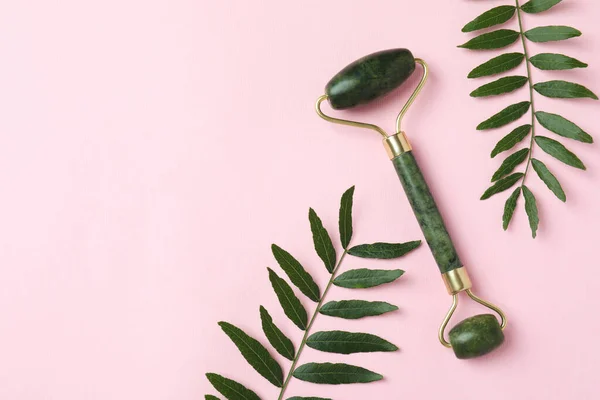 stock image Green face roller and leaves on pink background