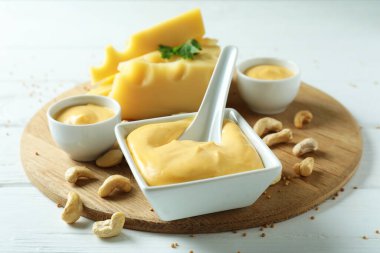 İçinde peynir sosu ve beyaz ahşap masa malzemeleri olan bir tahta.