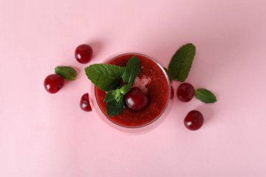 Bir bardak vişneli buzlu içecek ve pembe arka planda malzemeler.
