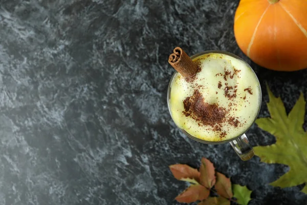 Bir bardak balkabaklı latte, balkabağı ve siyah dumanlı masada yapraklar.